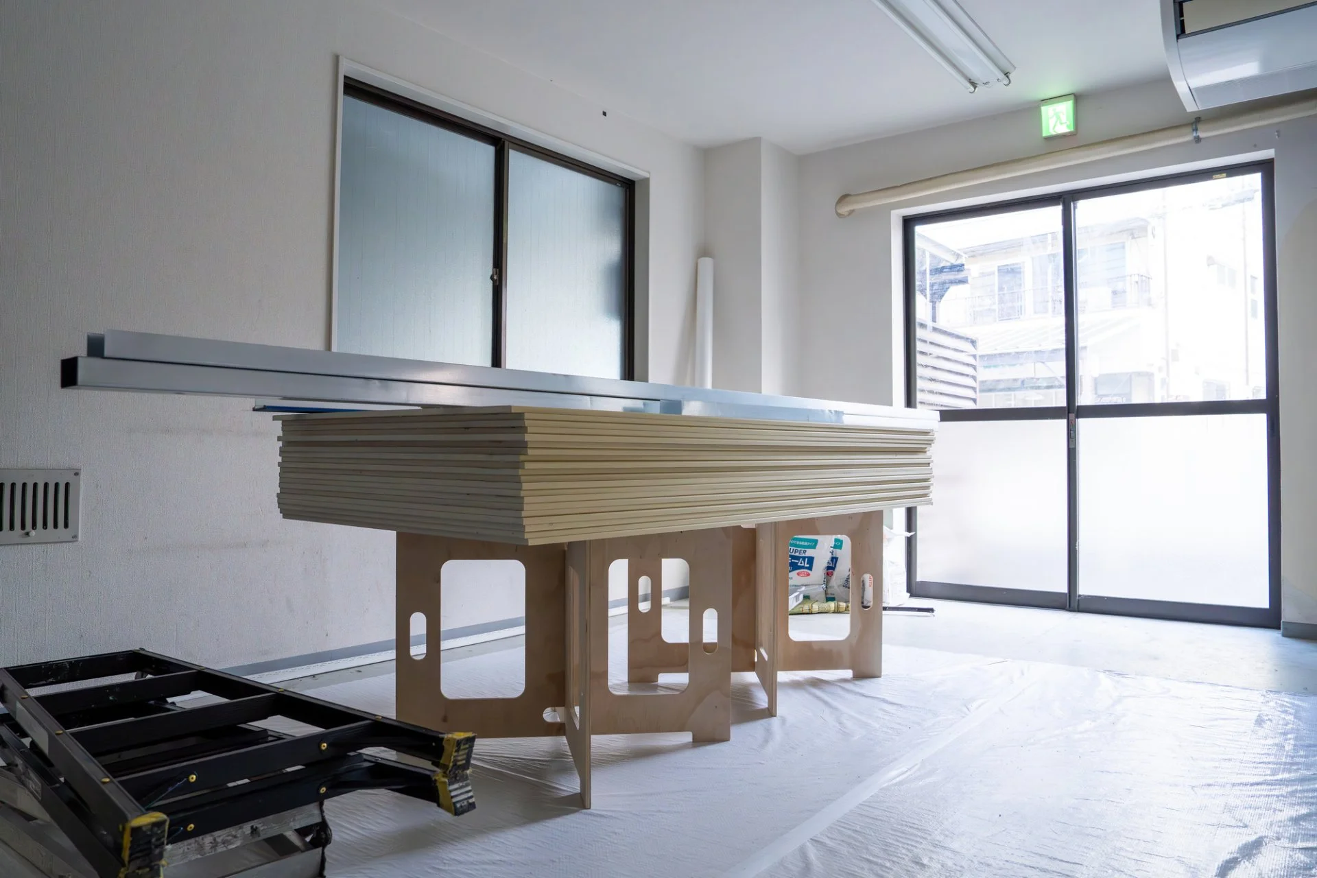白い壁紙を張り替えた室内で床材の補修を進める途中、資材と工具が整えられた内装現場の写真